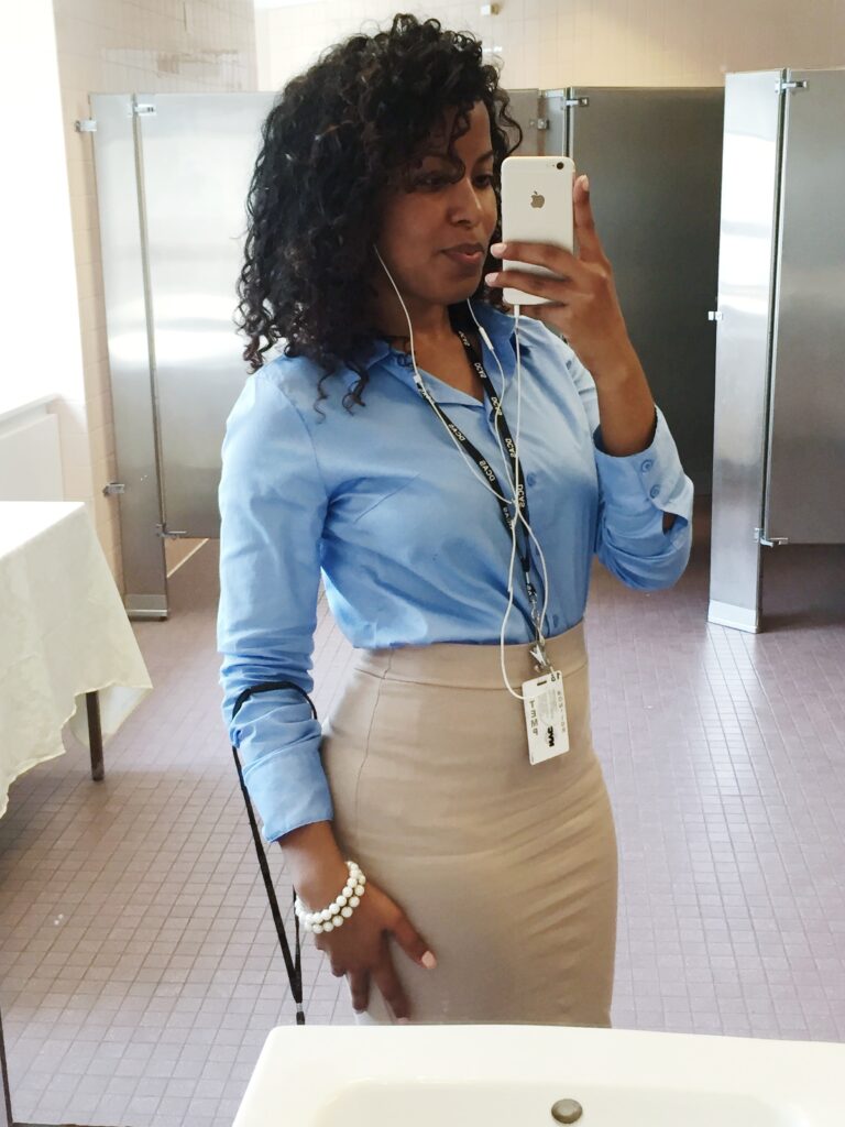 Mirror selfie of a woman wearing a blue shirt and pencil skirt, flaunting full, healthy natural curls and professional style.