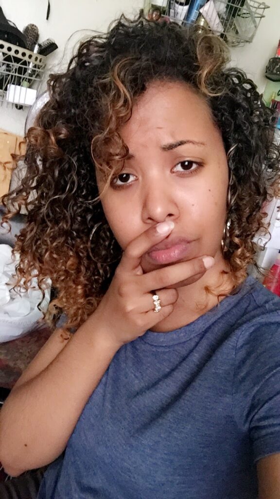 Woman looking concerned while touching her lips, showing damaged blonde curls and uneven curl pattern.