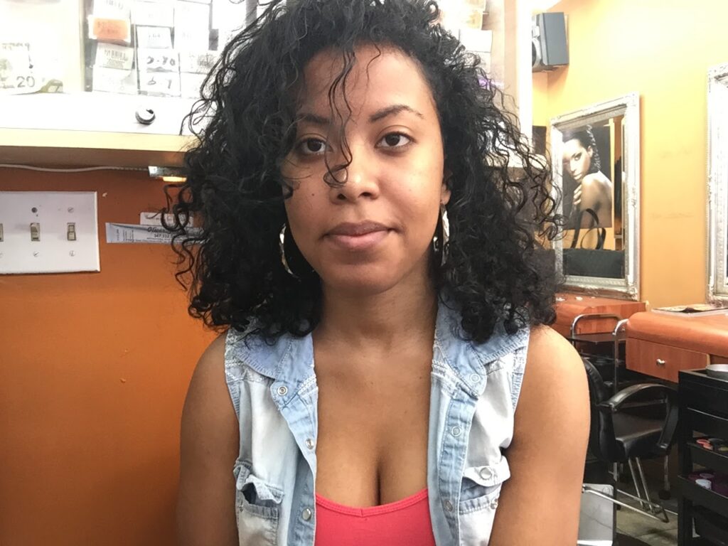 Woman with mid-length natural curls sitting in a salon, showing hair texture and growth after transition.