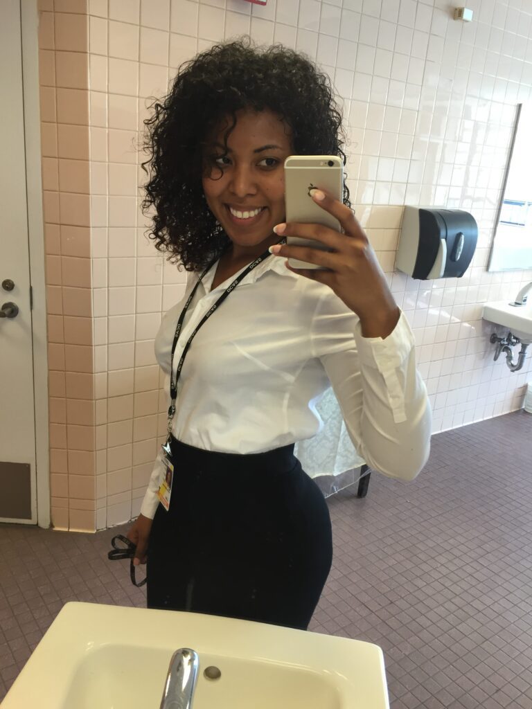Mirror selfie of a woman with defined curly hair in business attire, showing confidence and hair progress.