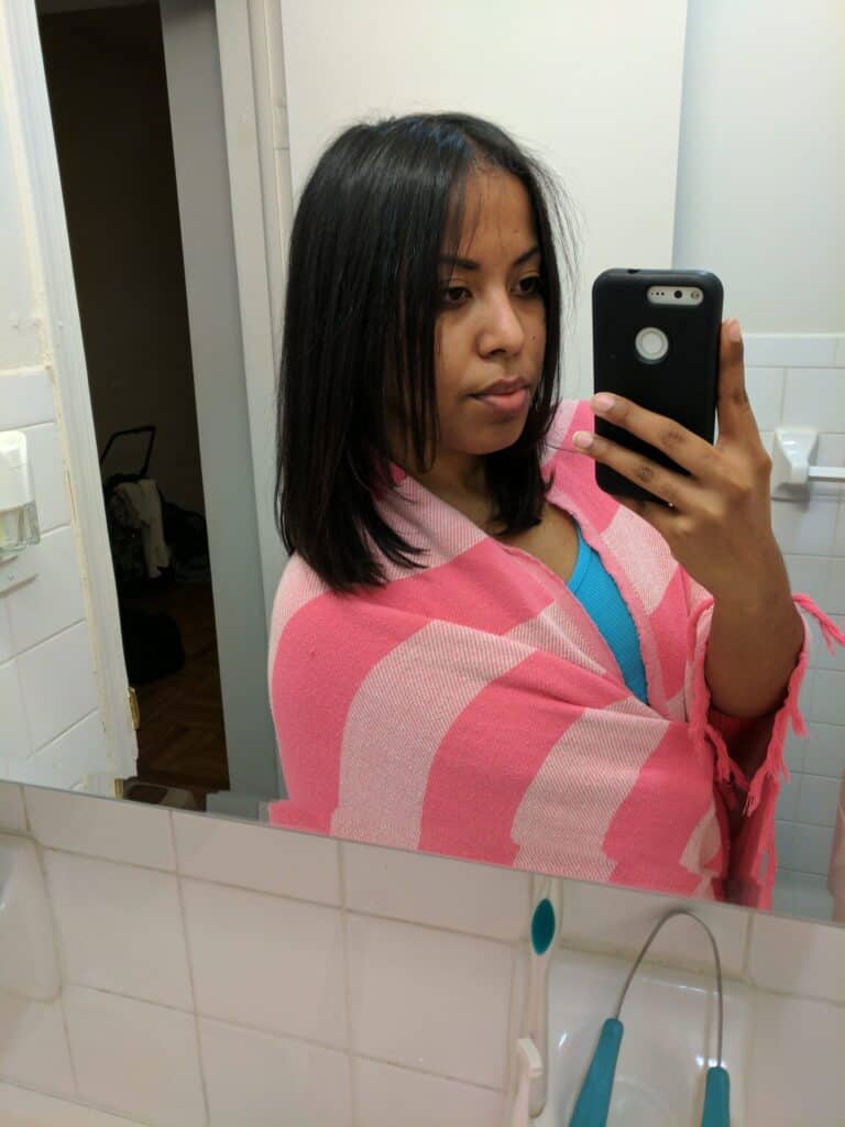 Woman with sleek, straightened shoulder-length hair in a pink and red striped sweater, taking a mirror selfie in a bathroom.