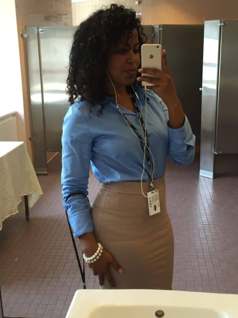 Mirror selfie of a woman wearing a blue shirt and pencil skirt, flaunting full, healthy natural curls and professional style.
