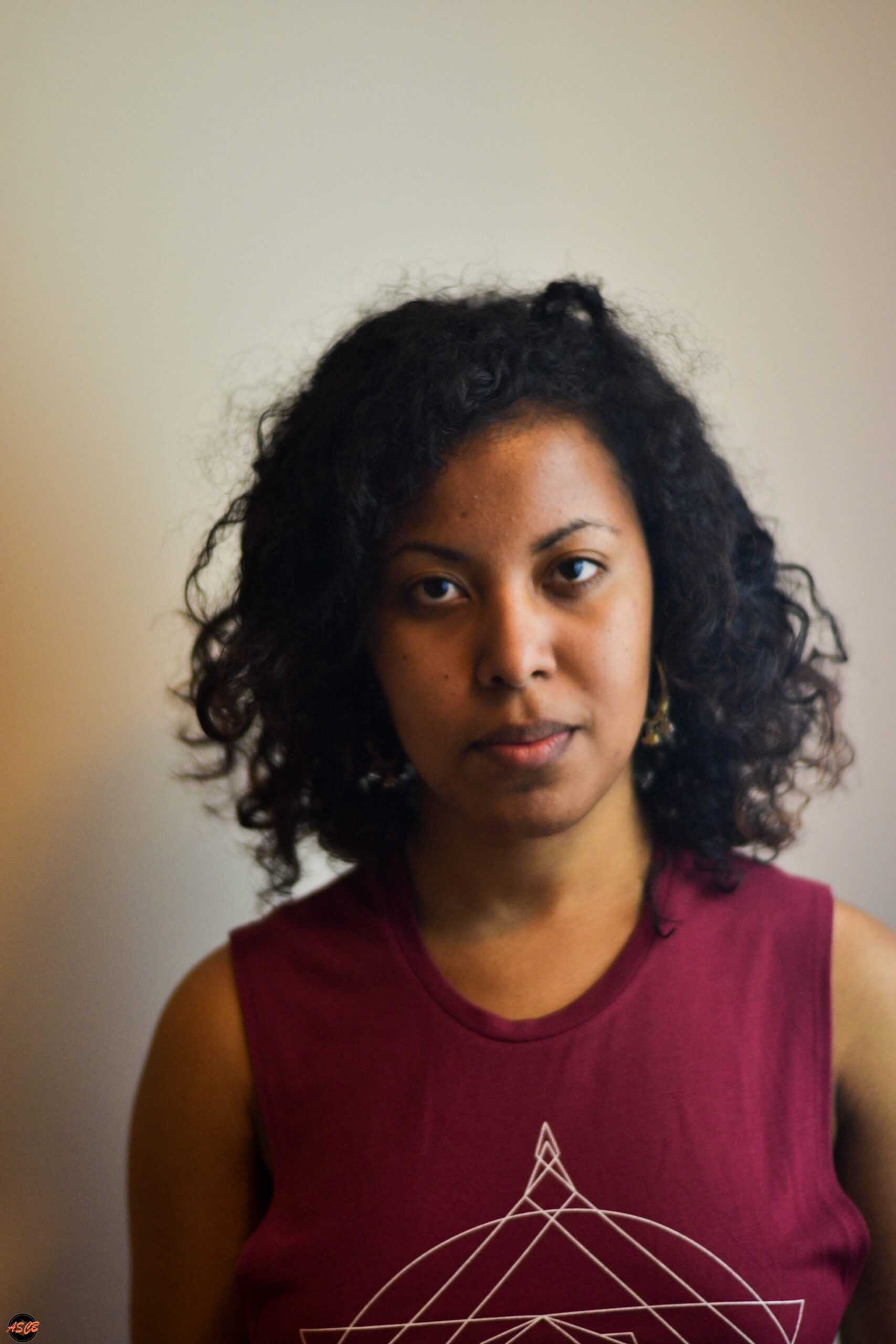 Smiling woman with natural curly hair wearing a maroon tank top, showcasing healthy curls in natural lighting.