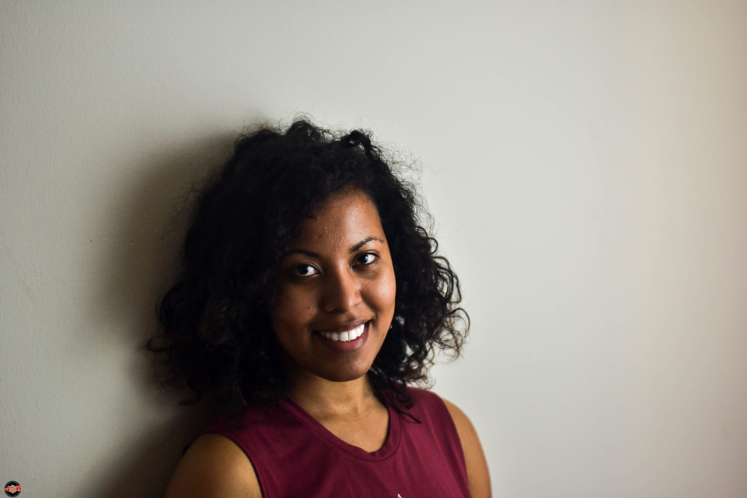 Woman with loosely defined curls and a serious expression, wearing a geometric tank top, posing against a neutral background.