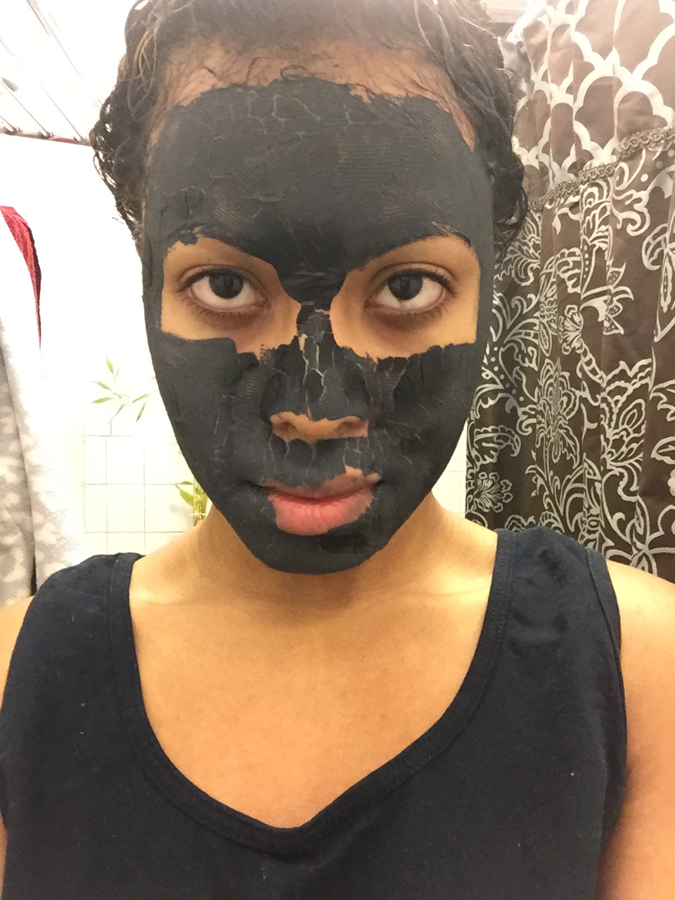 Close-up of a woman wearing a black bentonite clay face mask, showing full-face application for natural skincare detox.