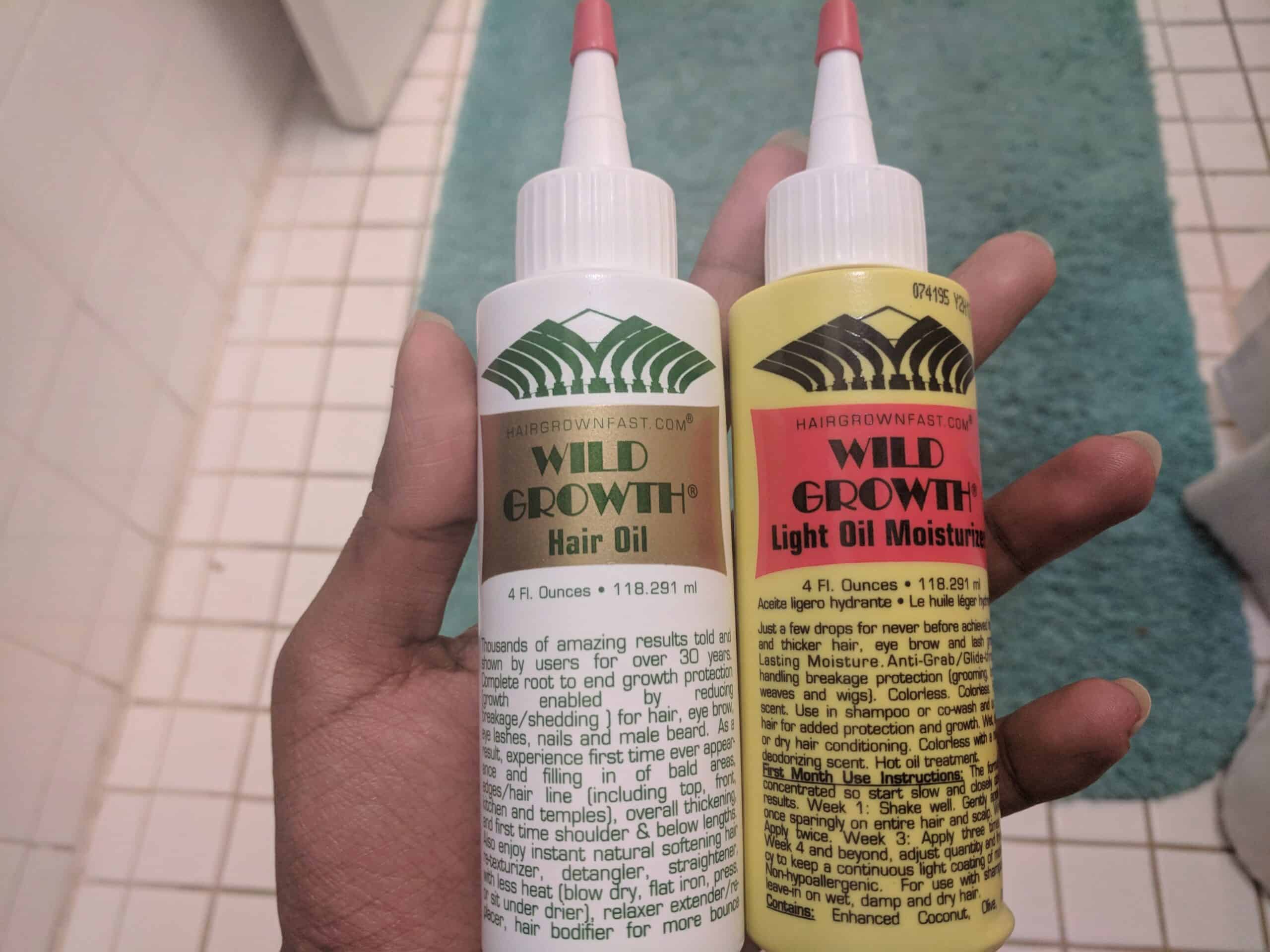 Close-up of a hand holding two bottles of Wild Growth hair oils—one original formula in a white bottle and one light oil moisturizer in a yellow bottle—used to support hair growth, reduce breakage, and add moisture.