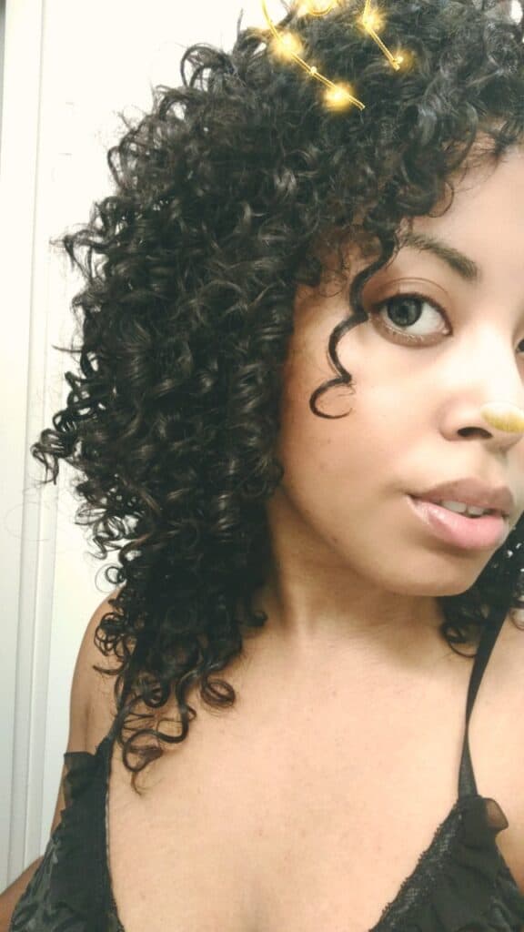 Close-up of a woman’s face and shoulder-length curls, showing enhanced definition and shine after a henna hair treatment.