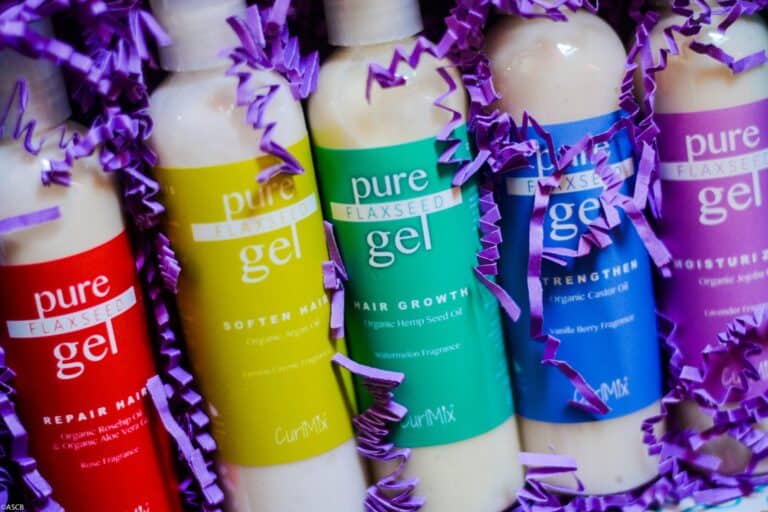 Close-up of five colorful CurlMix Pure Flaxseed Gel bottles—Repair, Soften, Hair Growth, Strengthen, and Moisturize—surrounded by purple crinkle paper.