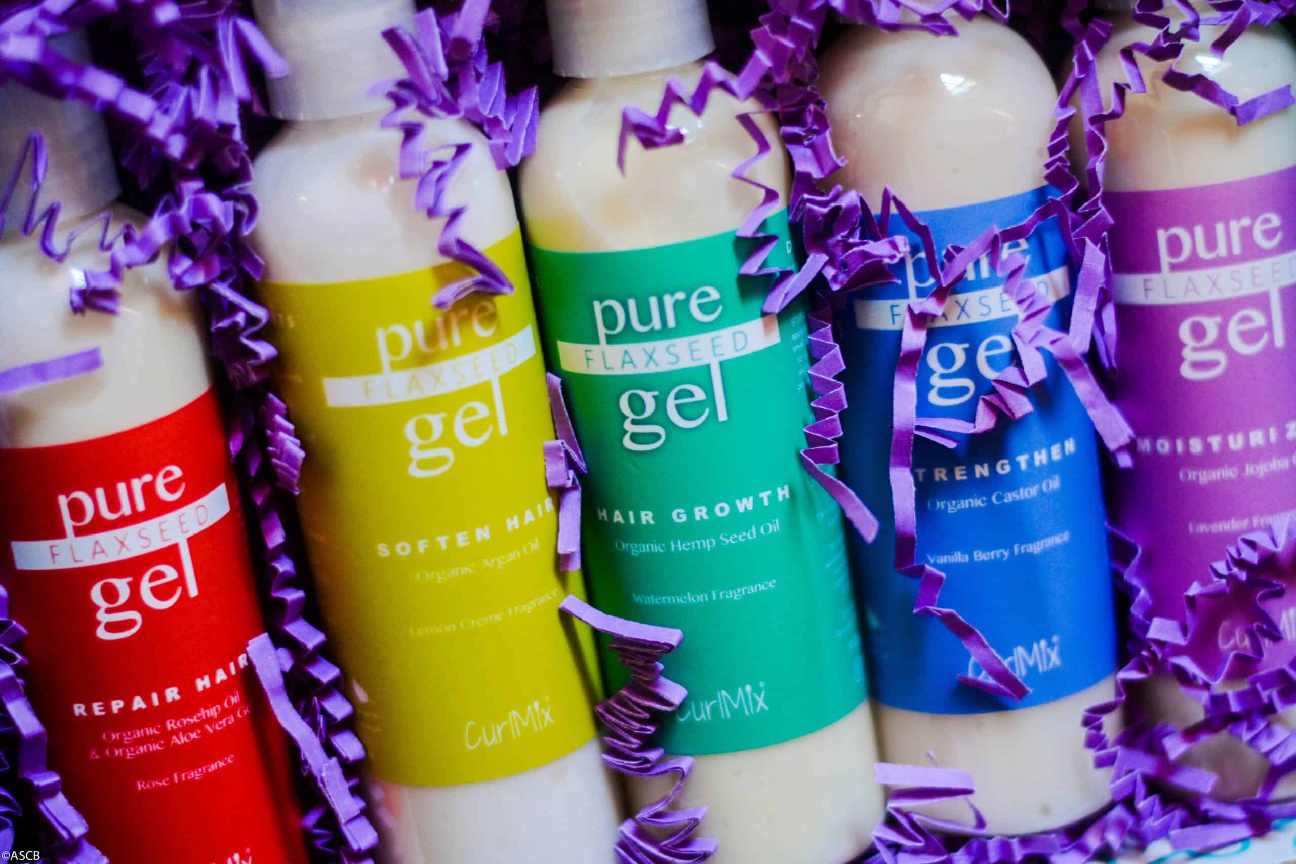 Close-up of five colorful CurlMix Pure Flaxseed Gel bottles—Repair, Soften, Hair Growth, Strengthen, and Moisturize—surrounded by purple crinkle paper.