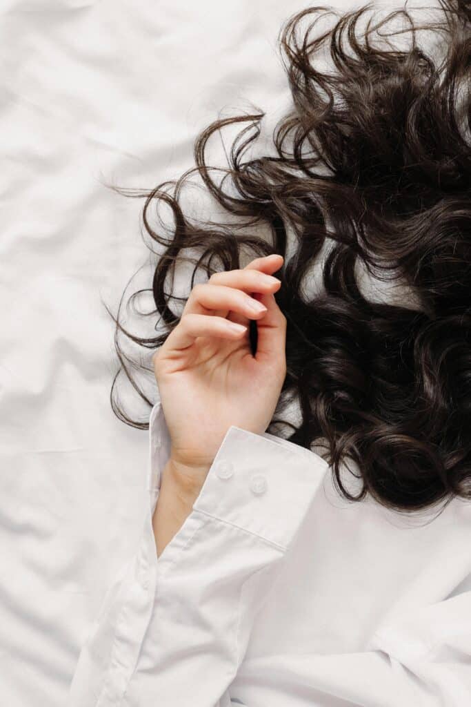Close-up of dark fine wavy hair resting on a white sheet, showing natural curl pattern and shine.