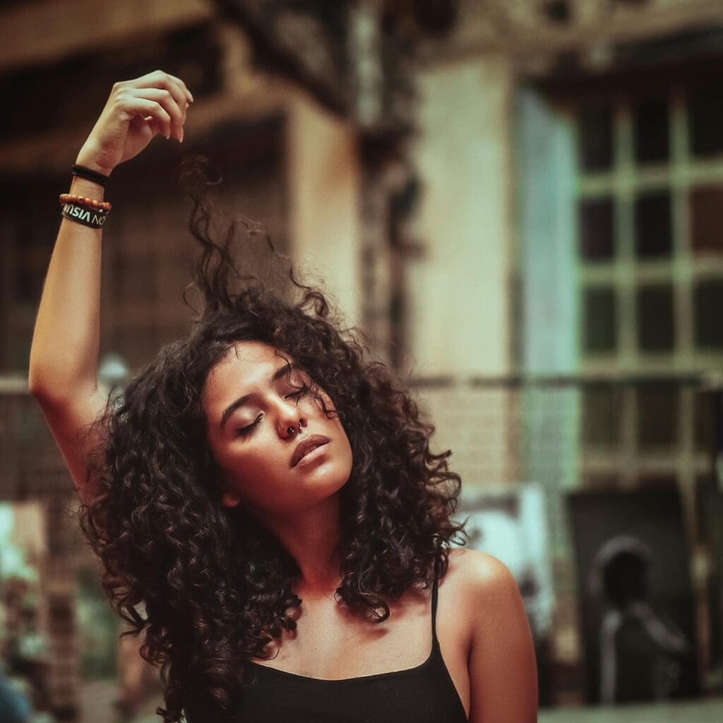 Woman with voluminous 3A curly hair lifting a curl, showing layered haircut shape that enhances definition and volume.