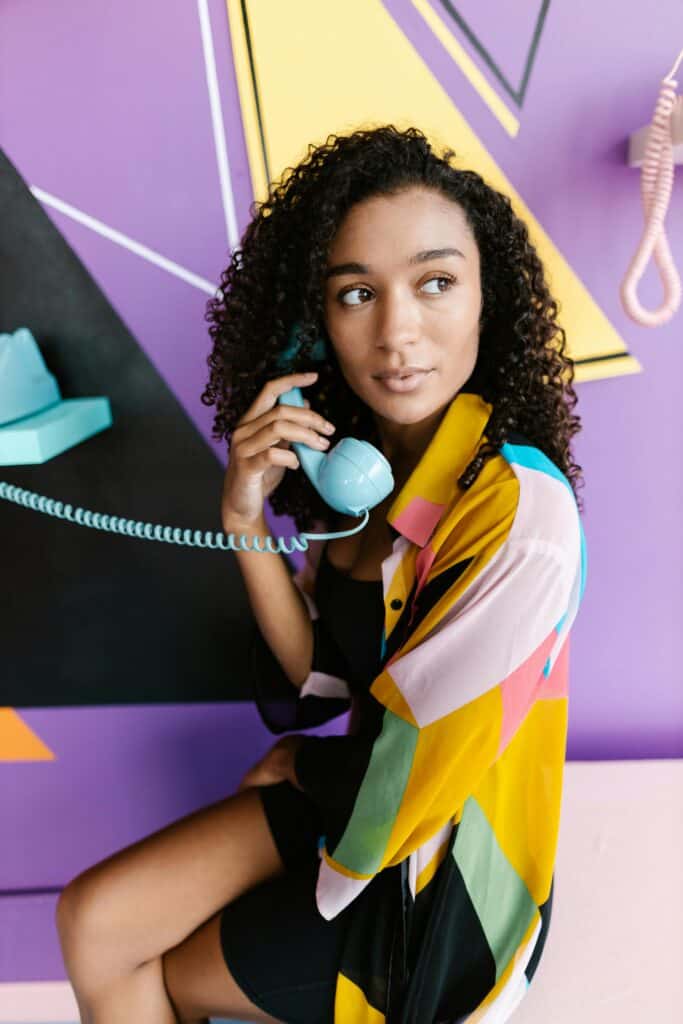 Woman with blonde 3B curls lying on a bed wearing a white shirt, looking to the side.