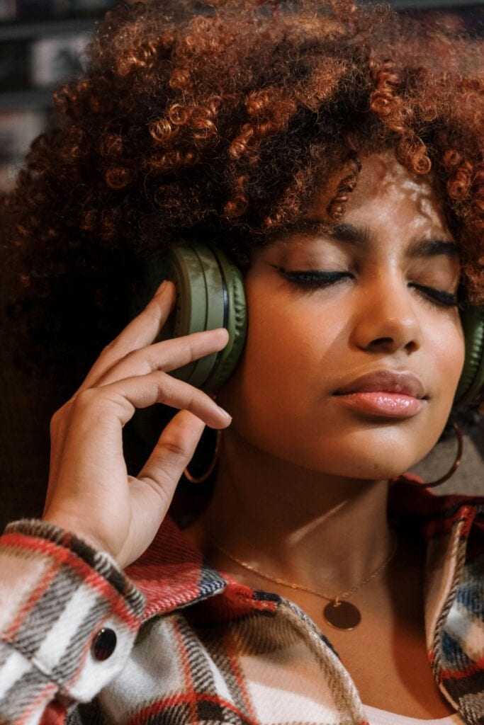 Woman with 3B curly hair wearing headphones and a plaid shirt, enjoying music with eyes closed.