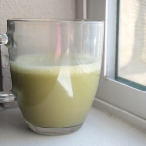 Homemade Jade Leaf matcha latte in a clear glass mug by a window, showing the creamy frothy top and light green color.