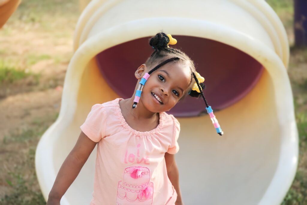 School-age girl with a protective hairstyle smiling while playing on a playground, illustrating healthy hair habits for active children.