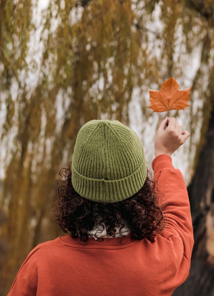 Person with curly hair wearing a knit beanie outdoors during fall.